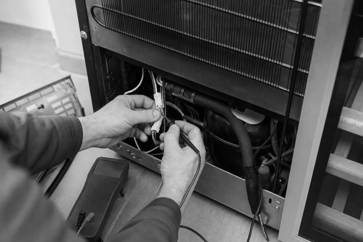 Black-and-white close-up of a meter probe on a wiring connector inside the open base of a refrigerator